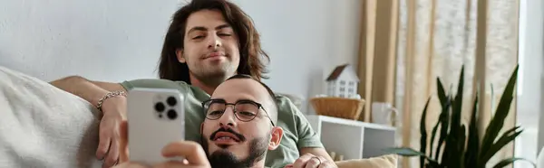 Two men relax on a couch, one looking at his phone, the other leaning on him. — Stock Photo