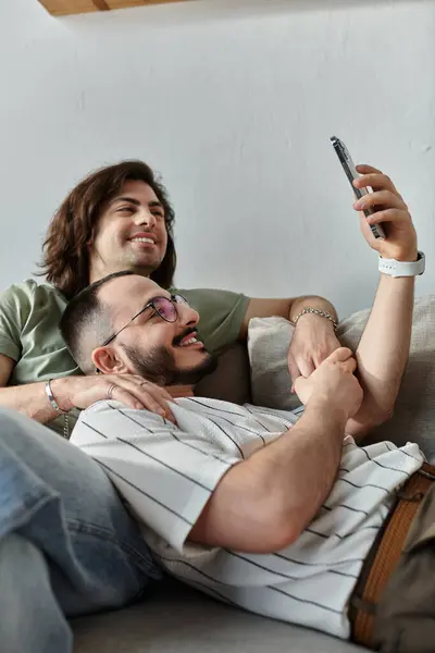 Deux hommes se détendent sur un canapé, riant en regardant un écran de téléphone. — Stock Photo