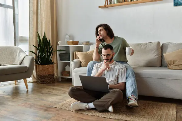 Due uomini si rilassano a casa, uno sul divano, l'altro sul pavimento con un computer portatile. — Foto stock