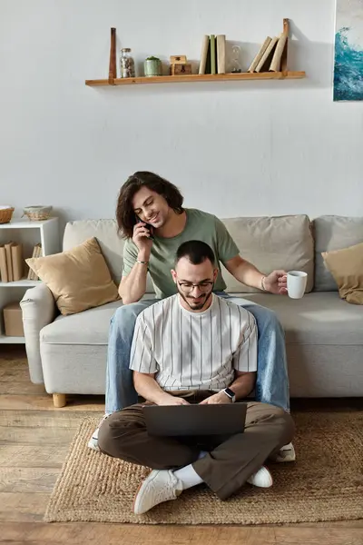 A couple relaxes at home, one working on a laptop while the other enjoys coffee and a phone call. — Stock Photo