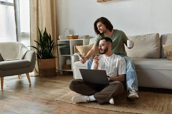 Una coppia si siede sul pavimento, un uomo usa un portatile mentre l'altro guarda il suo telefono.. — Foto stock