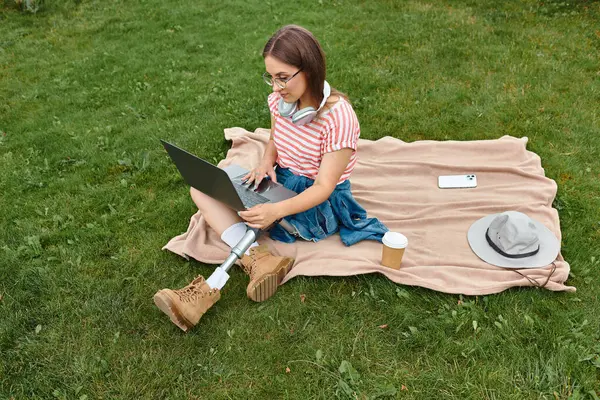 Eine junge Frau mit Beinprothese arbeitet in einem Park an ihrem Laptop. — Stockfoto