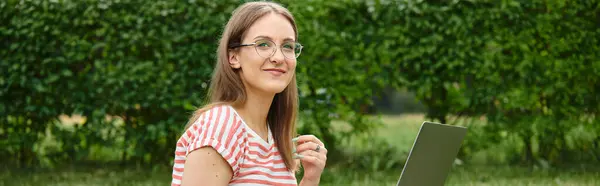 Молодая женщина улыбается, используя свой ноутбук на открытом воздухе. — стоковое фото