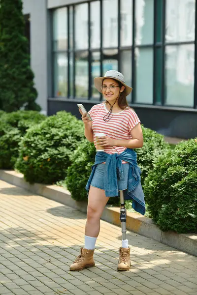 A young woman with a prosthetic leg smiles as she walks through a park on a sunny day. — Stock Photo