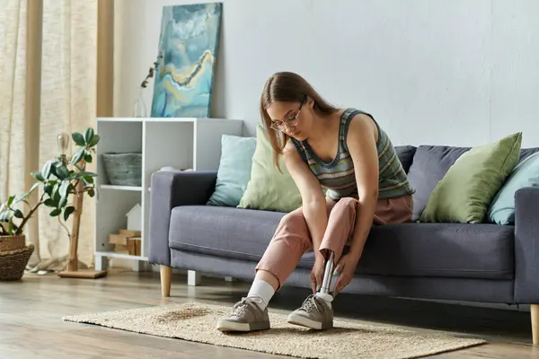 Eine junge Frau sitzt auf einer Couch in ihrem Wohnzimmer und justiert die Beinprothese, die sie trägt. — Stockfoto