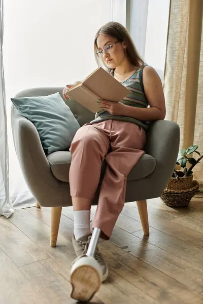 Una giovane donna con una gamba protesica siede su una poltrona di peluche, avvolta in un libro. — Stock Photo