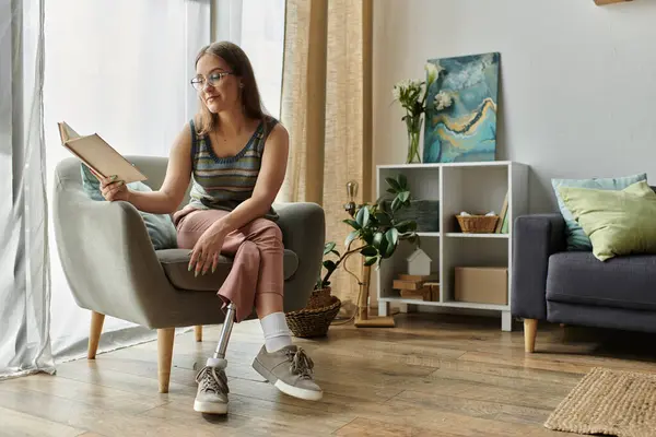 A young woman with a prosthetic leg relaxes in her living room, engrossed in a book. — Stock Photo