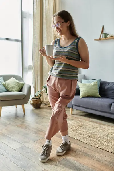 A young woman with a prosthetic leg smiles as she enjoys a cup of coffee in her modern living room. — Stock Photo