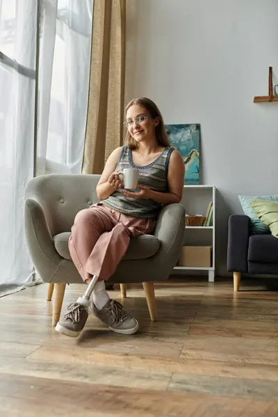 A young woman with a prosthetic leg enjoys a cup of coffee in her modern living room. — Stock Photo