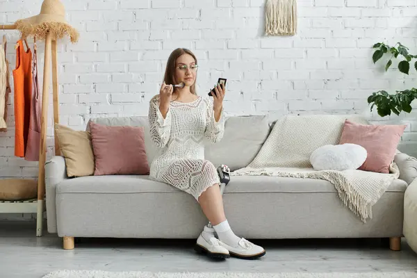 A young woman with a prosthetic leg sits on a couch in her home, applying makeup while looking in a mirror. — Stock Photo
