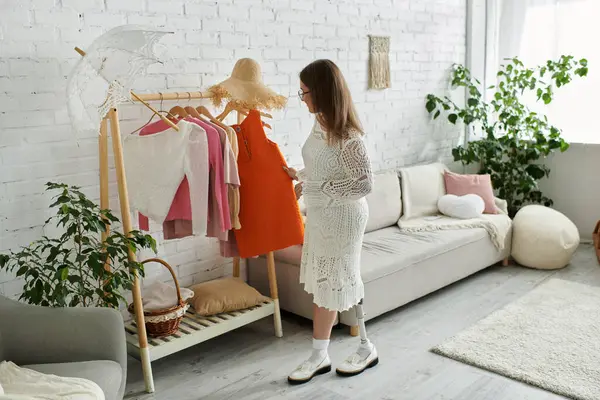 Une jeune femme avec une jambe prothétique se tient devant un porte-vêtements, choisissant une robe orange à porter. — Photo de stock