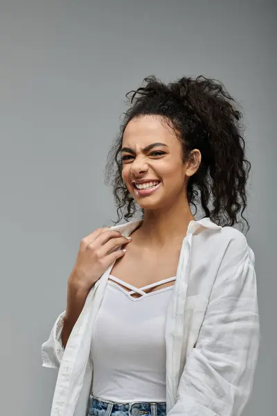 A young woman with curly hair, wearing a white shirt and smiling brightly against a grey background. — Stock Photo