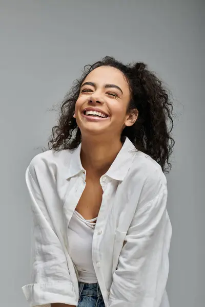 Uma jovem mulher com cabelo encaracolado ri contra um pano de fundo cinza, sua alegria irradiando através da imagem. — Fotografia de Stock