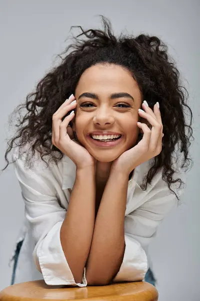 Una joven afroamericana con el pelo rizado sonríe radiantemente, con las manos apoyadas en la barbilla. — Stock Photo