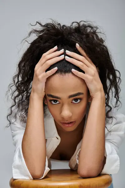 Une jeune femme noire aux cheveux bouclés pose sa tête sur ses mains, regardant vers le bas avec réflexion. — Photo de stock