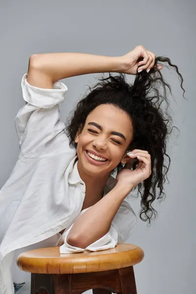 A young African American woman poses with a big smile, her curly hair tousled, against a grey backdrop. — Stock Photo