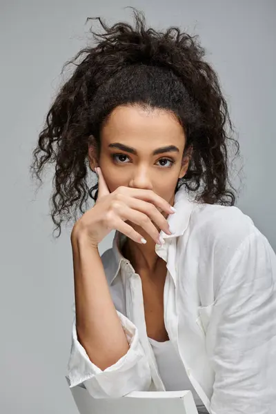 A young woman with curly hair poses in a white shirt against a grey background. — Stock Photo