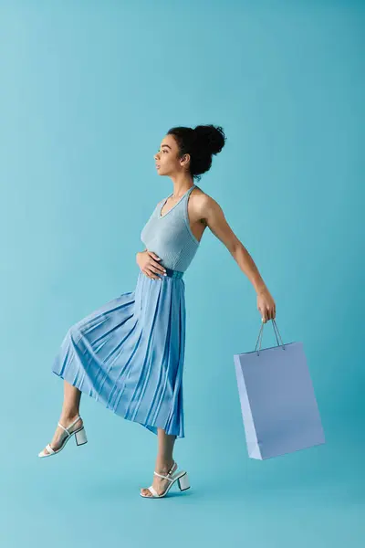 A young woman happily struts in a blue dress with a shopping bag, expressing joy in shopping and embracing her style — Stock Photo