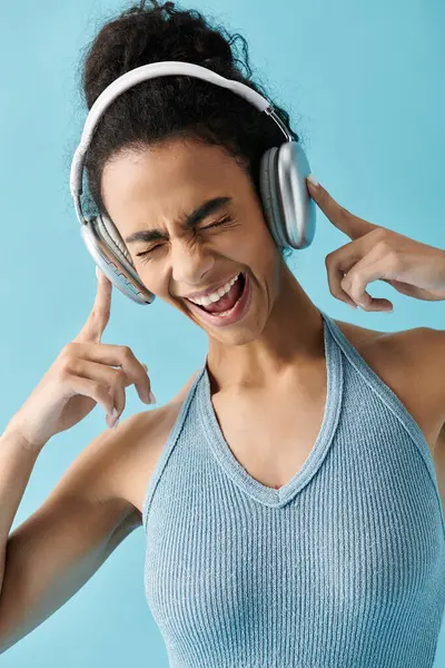 Una giovane donna afroamericana con la canotta blu canta con le cuffie, gli occhi chiusi e un'espressione gioiosa. — Foto stock