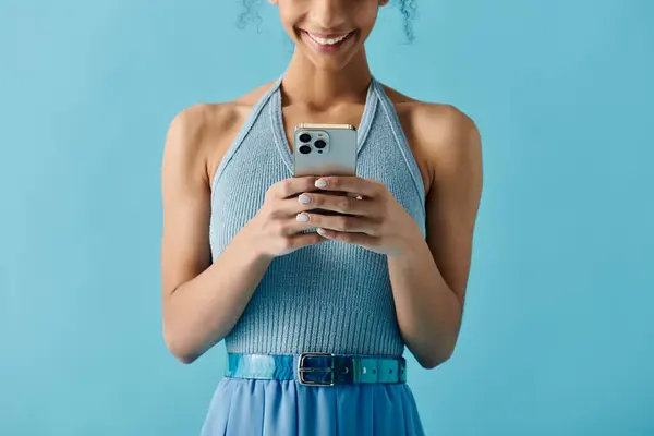 A young woman in a blue dress smiles as she uses her phone, showcasing a vibrant and joyful expression. — Stock Photo