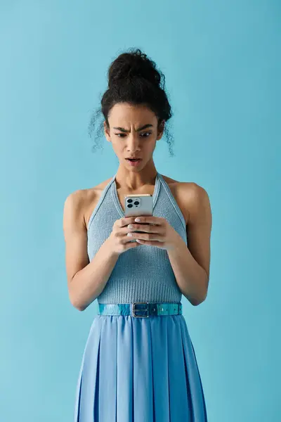 Uma jovem mulher em um vestido azul parece chocada enquanto lê uma mensagem em seu telefone. — Fotografia de Stock