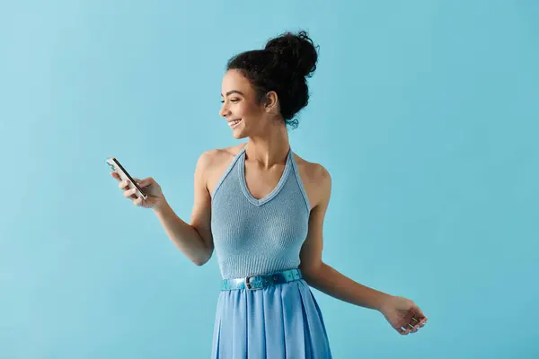 A beautiful young woman in a blue dress smiles while scrolling on her phone. — Stock Photo