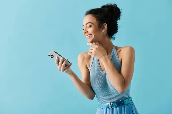 A young African American woman wearing a blue dress smiles as she looks at her smartphone. — Stock Photo
