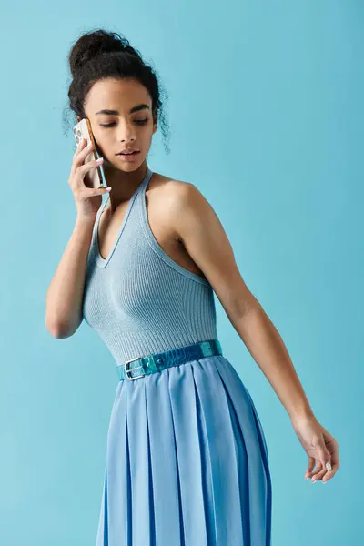 Eine junge Frau in blauem Kleid und Gürtel telefoniert vor blauem Hintergrund. — Stockfoto