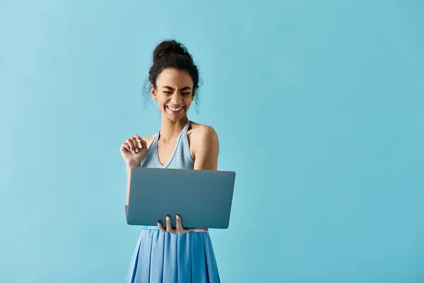 Eine junge Afroamerikanerin im blauen Kleid lächelt, während sie auf ihren Laptop blickt. — Stockfoto