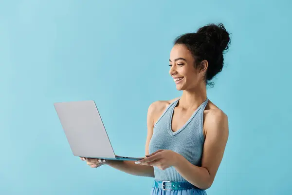 A young African American woman in a blue dress holds a laptop, smiling at the screen. — Stock Photo