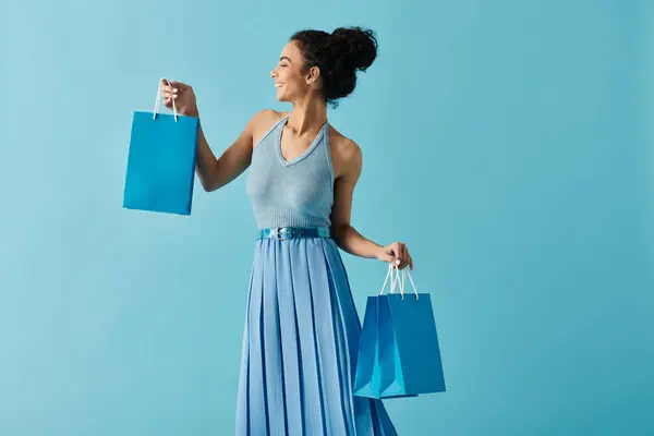 Uma jovem mulher em um vestido azul sorri brilhantemente enquanto carrega sacos de compras. — Fotografia de Stock