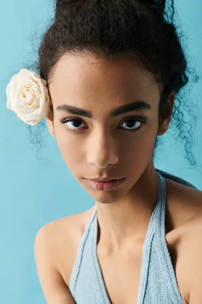 Uma jovem mulher com cabelo preto encaracolado e uma flor branca em seu cabelo olha intensamente para a câmera. — Fotografia de Stock