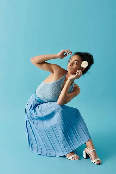 Uma jovem mulher senta-se graciosamente em um fundo azul, seu vestido em cascata em torno dela como uma onda. — Fotografia de Stock