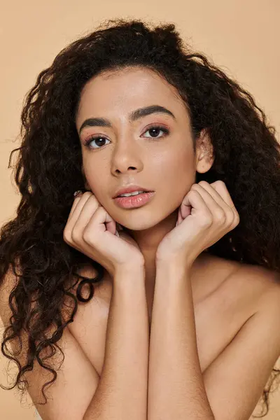 Una giovane donna con i capelli ricci e le spalle nude guarda direttamente lo spettatore con un'espressione calma e composta. — Foto stock