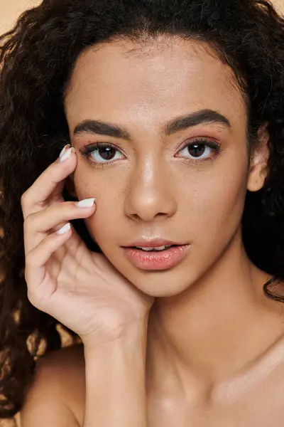 Una giovane donna con i capelli ricci e trucco naturale fissa direttamente la fotocamera, con la mano appoggiata sulla guancia. — Foto stock