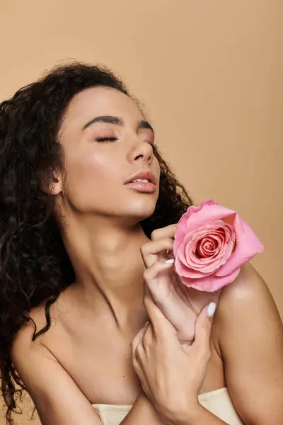 Una giovane donna afroamericana con il trucco naturale tiene una rosa, gli occhi chiusi, apparentemente inalando il suo profumo. — Foto stock