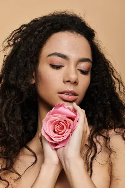 A young woman with long, curly hair holds a pink rose close to her face, her eyes closed in contemplation. — Stock Photo