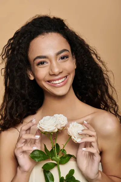 A young African American woman with curly hair smiles brightly while holding a bouquet of white roses. — Stock Photo
