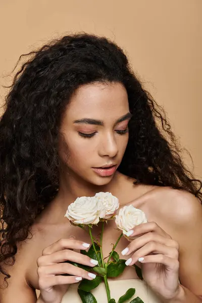 Uma jovem com cabelos longos encaracolados segura rosas brancas, olhando para elas com um sorriso gentil.. — Fotografia de Stock