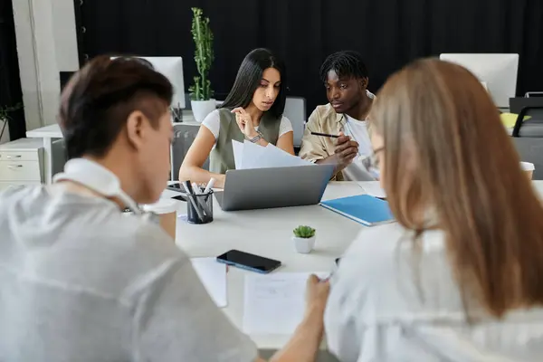A team of four diverse individuals works together on a project in a contemporary office setting. — Stock Photo