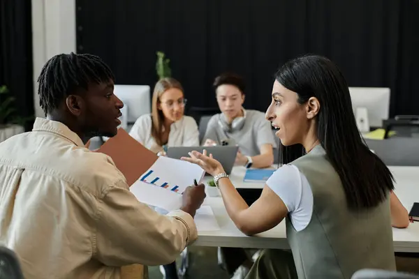 A diverse team of startup employees brainstorm over graphs and charts. — Stock Photo