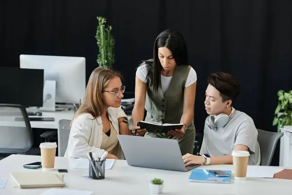 Una donna indica un notebook mentre due colleghi lavorano su un computer portatile. — Foto stock