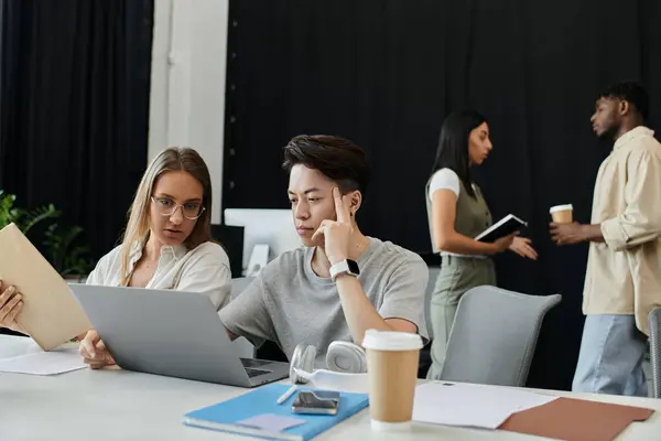 Two coworkers collaborate on a laptop, with a third looking on in an office — Stock Photo