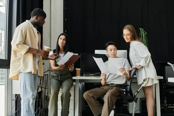 Four colleagues collaborate and review documents while standing around a desk in a modern office. — Stock Photo