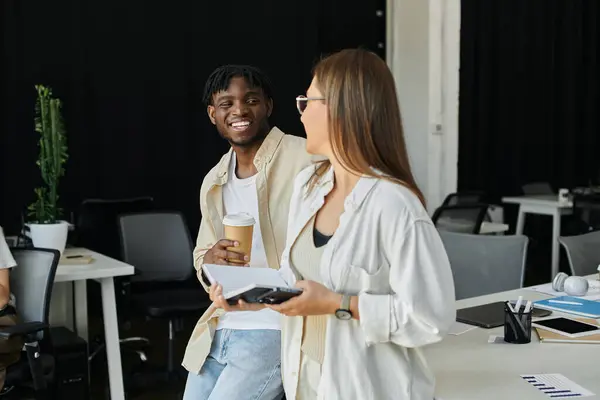 Two coworkers, one with a cup of coffee, smile at each other during a relaxed work moment. — Stock Photo