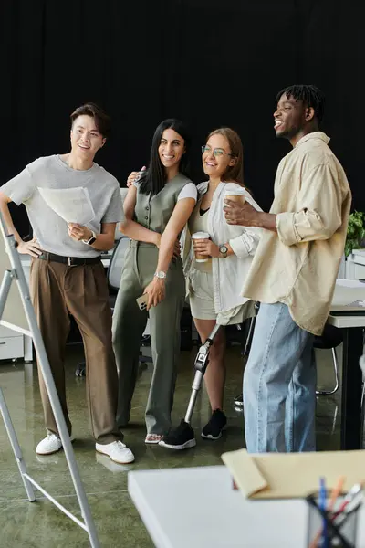 Une équipe diversifiée de quatre collègues se tient dans un bureau moderne, souriant et tenant des tasses à café. — Photo de stock