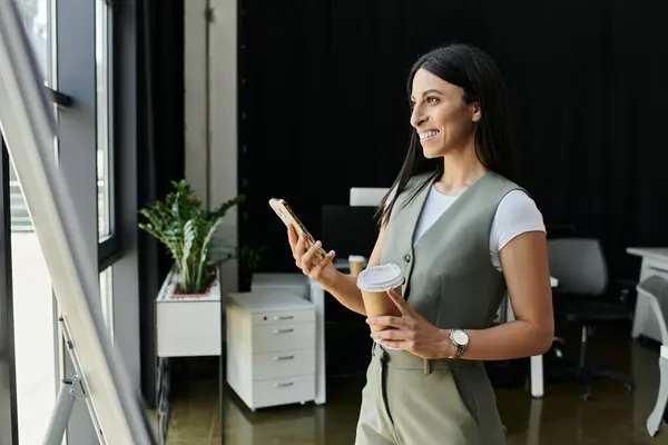 A businesswoman checks her phone while holding a coffee in her office. — Stock Photo