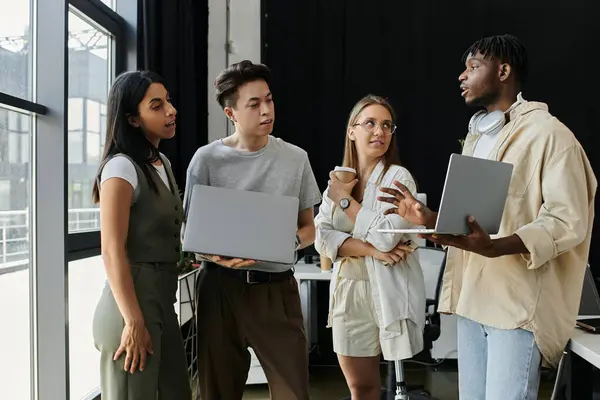 Un grupo de jóvenes emprendedores idean ideas, portátiles en mano, en un entorno de oficina moderno. - foto de stock