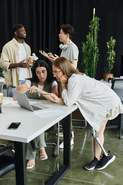 Two women work on a laptop at a table with a third person standing in the background. — Stock Photo