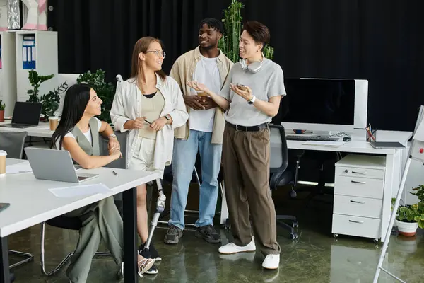 A group of four diverse colleagues stand in a modern office, engaged in a conversation. — Stock Photo